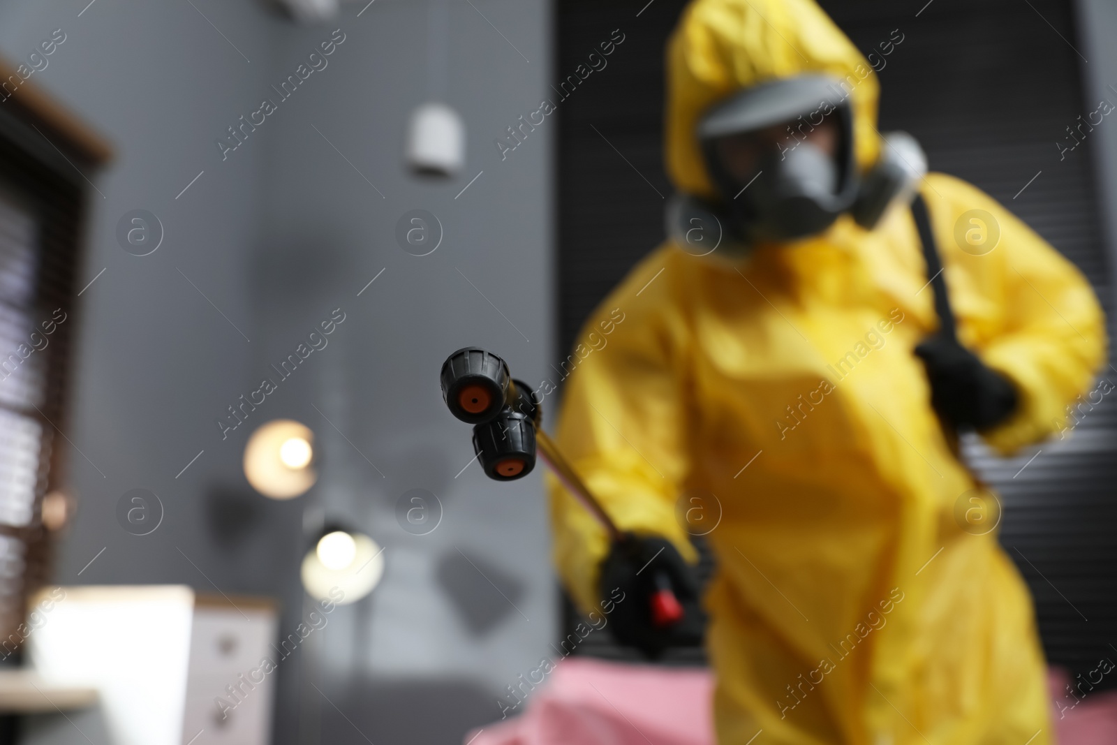 Photo of Pest control worker in protective suit indoors, focus on insecticide sprayer