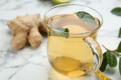 Diet herbal tea with green leaves and ginger on white marble table, closeup