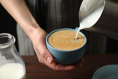 Woman pouring milk into cup of hot coffee, closeup