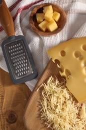 Photo of Grated, cut cheese and grater on wooden table, flat lay