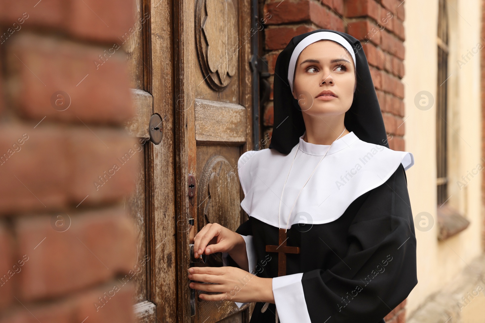 Photo of Young nun near wooden door of old building outdoors