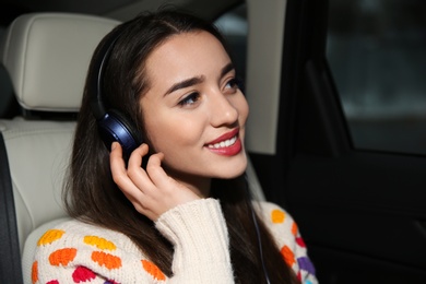 Photo of Beautiful young woman listening to music with headphones in car