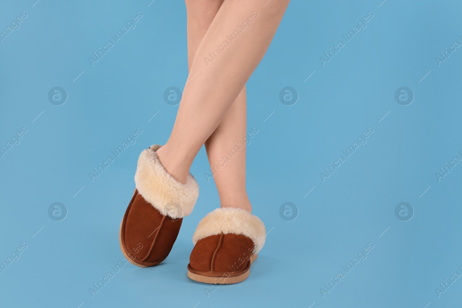 Photo of Woman in warm soft slippers on light blue background, closeup