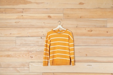 Hanger with stylish sweater on wooden background