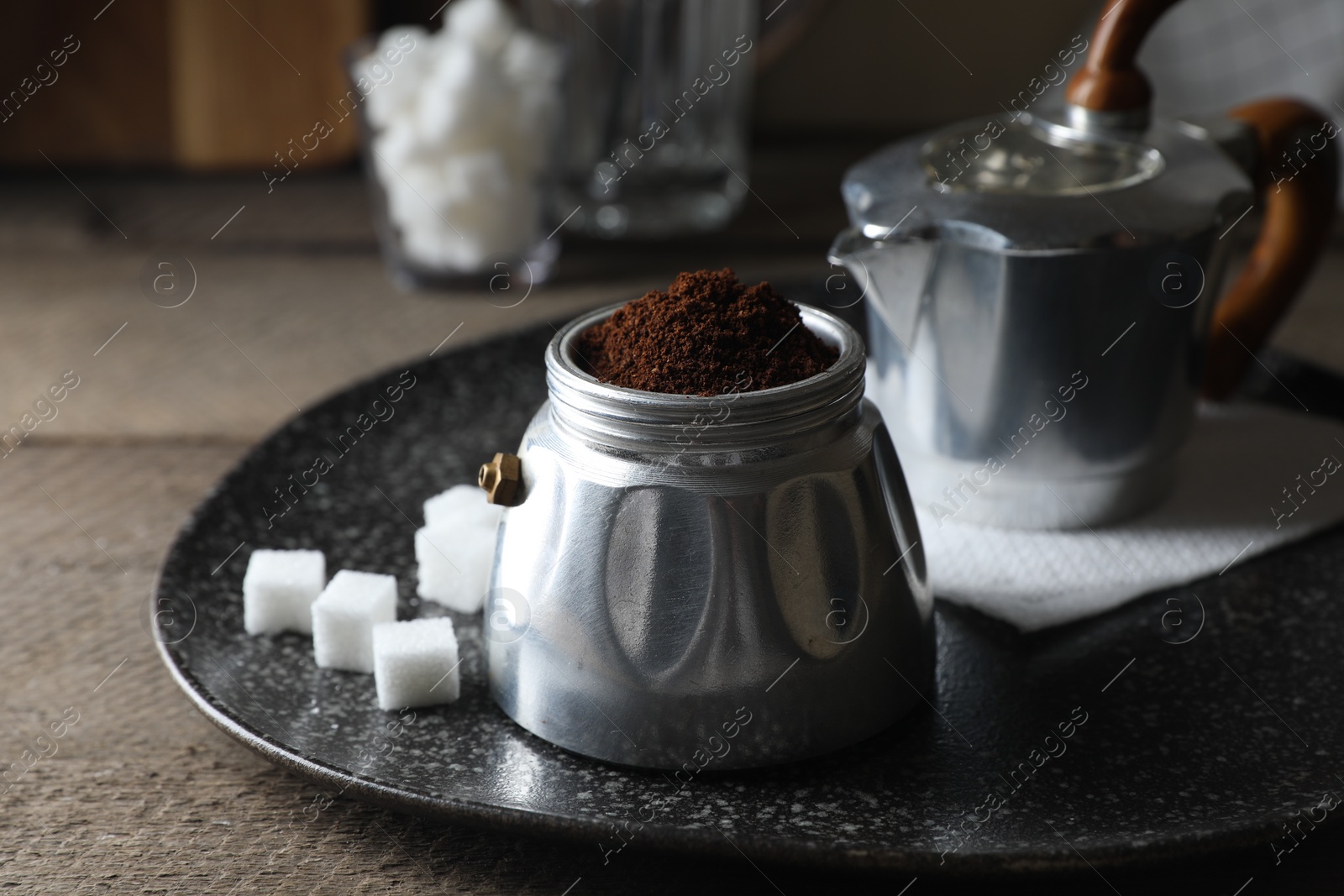 Photo of Ground coffee in moka pot and sugar cubes on wooden table, closeup