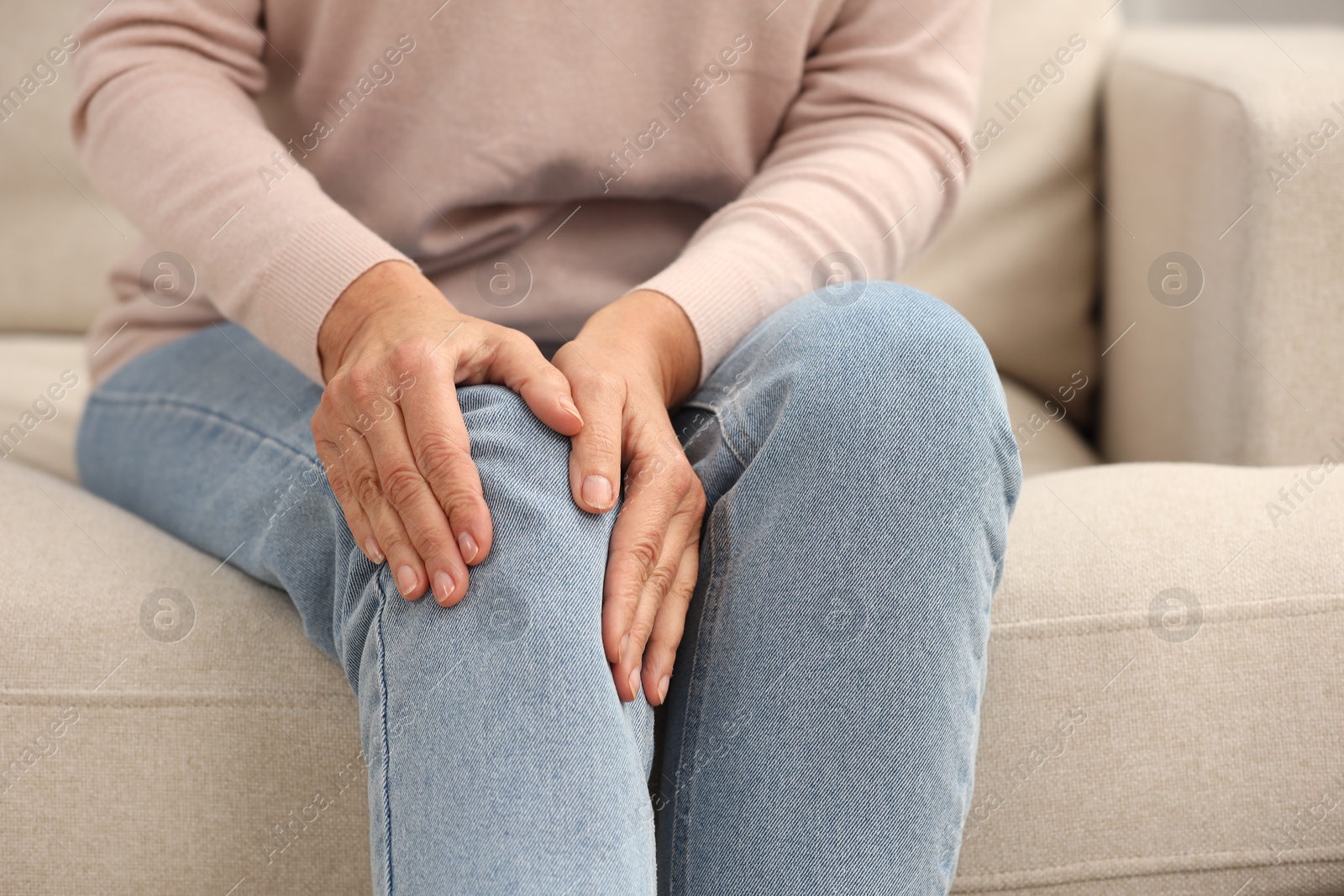 Photo of Mature woman suffering from knee pain on sofa, closeup. Rheumatism symptom