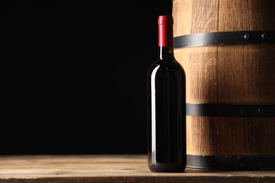 Photo of Bottle of delicious wine and wooden barrel on table against black background. Space for text