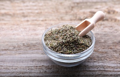 Photo of Glass bowl with dried thyme and scoop on wooden table, closeup