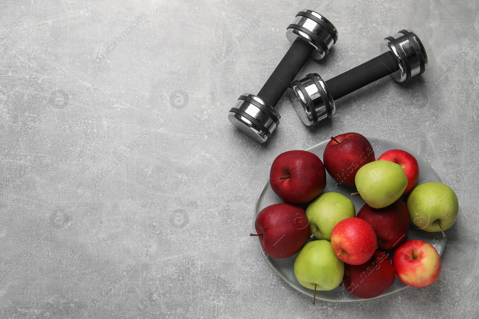 Photo of Healthy diet. Plate with apples and dumbbells on light grey textured table, flat lay. Space for text