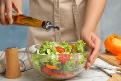 Photo of Woman dressing tasty fresh Greek salad with olive oil at white marble table, closeup