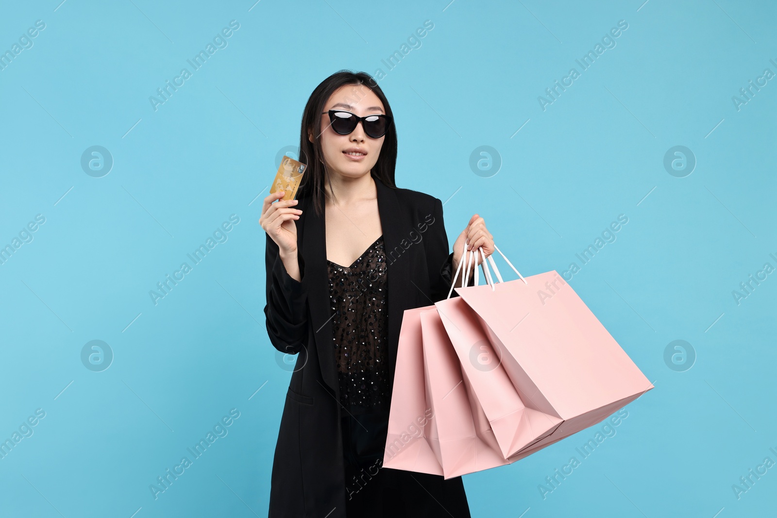 Photo of Smiling woman with shopping bags and credit card on light blue background