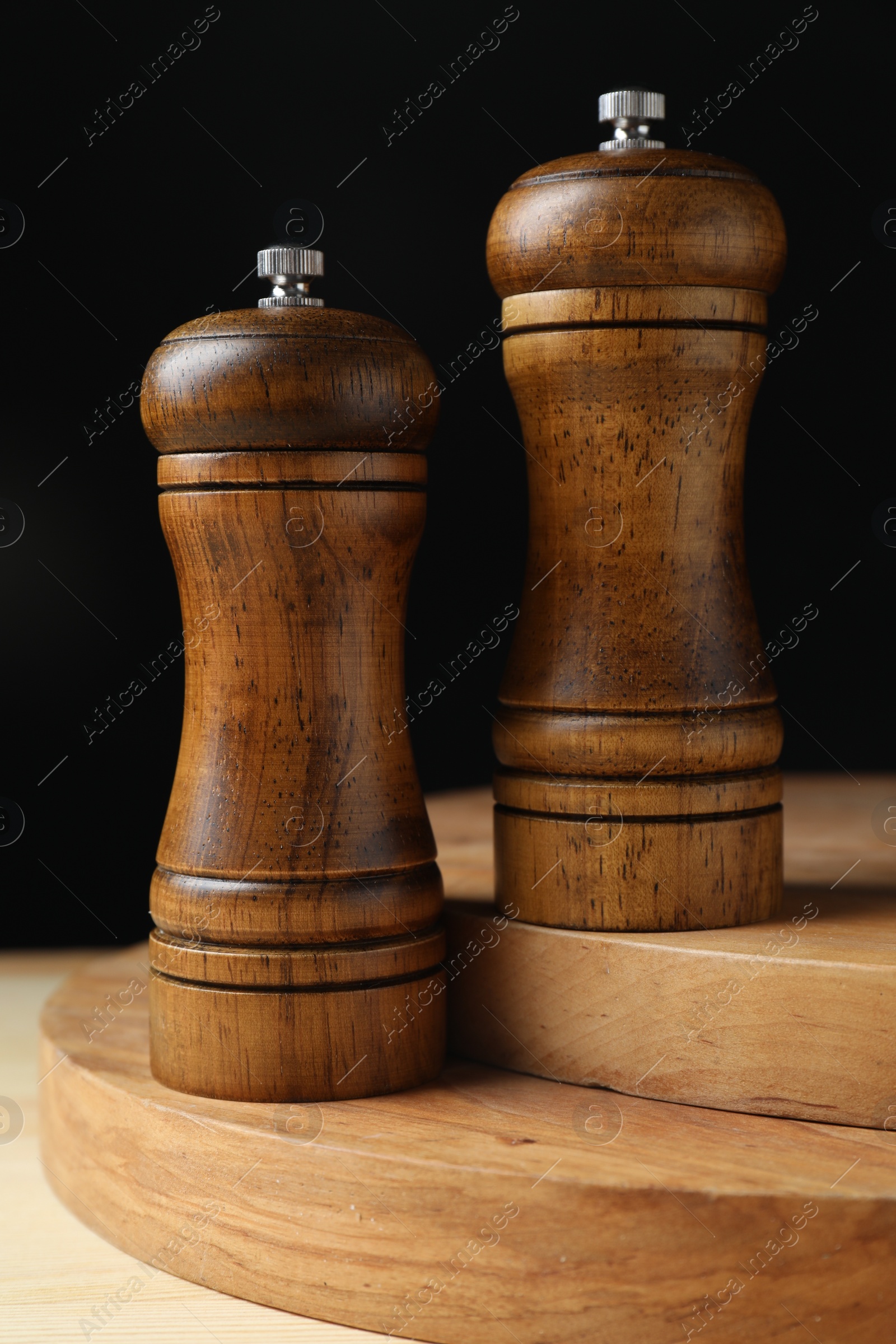 Photo of Salt and pepper shakers on wooden table against black background, closeup