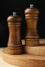 Photo of Salt and pepper shakers on wooden table against black background, closeup