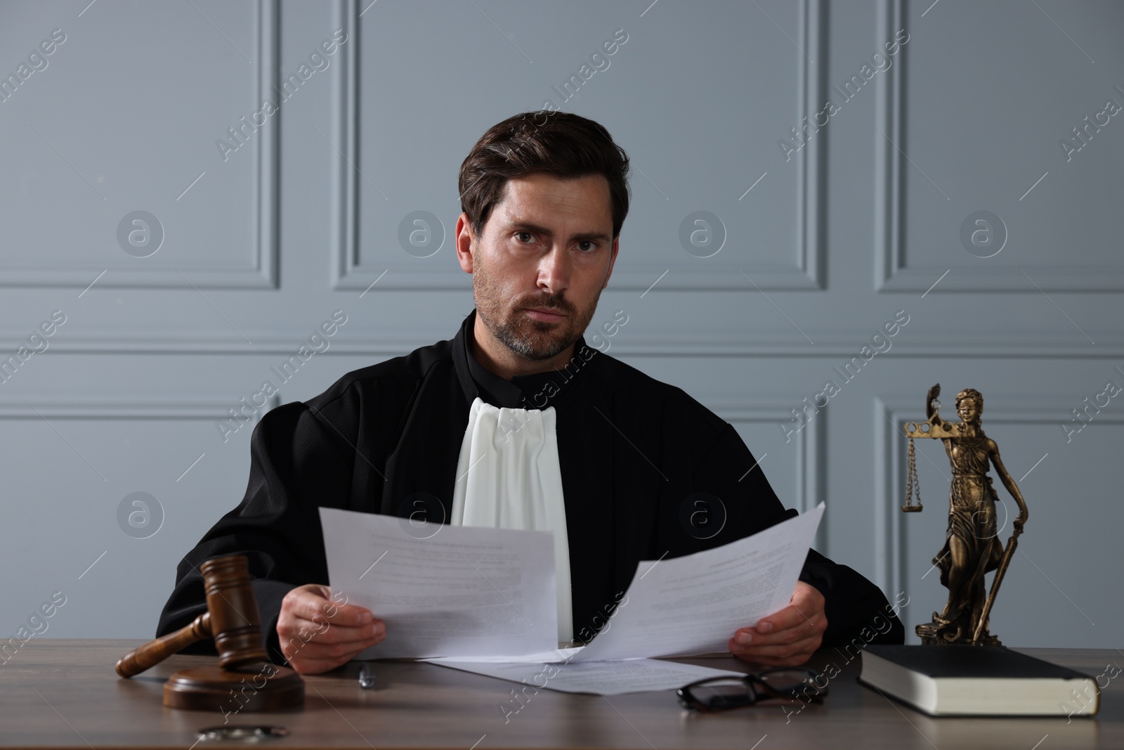 Photo of Judge with gavel and papers sitting at wooden table indoors