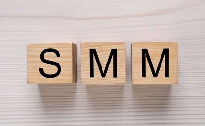 Photo of Cubes with abbreviation SMM (Social media marketing) on white wooden table, flat lay