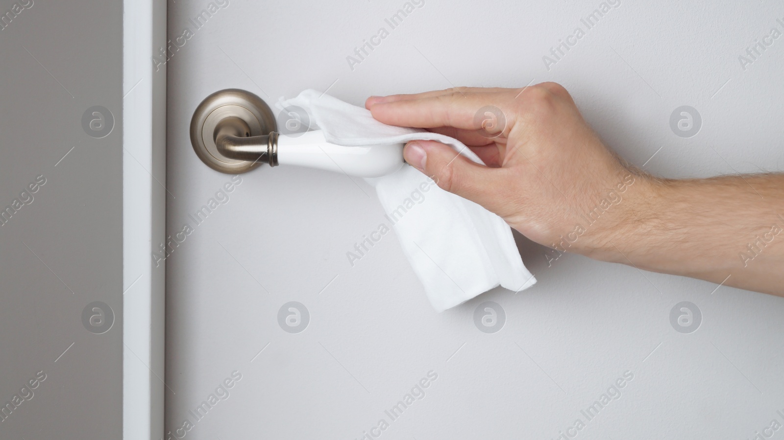 Photo of Man cleaning doorknob with wet wipe indoors, closeup. Protective measures