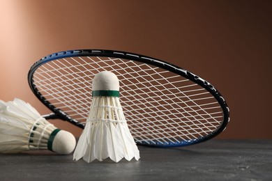 Photo of Feather badminton shuttlecocks and racket on grey table against brown background, closeup