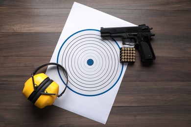Photo of Shooting target, handgun with bullets and headphones on wooden table, top view