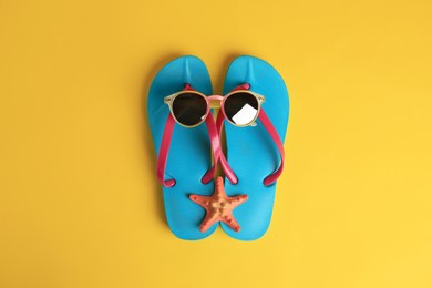 Photo of Flip flops, sunglasses and starfish on yellow background, flat lay. Beach accessories