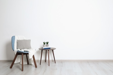 Photo of Stylish room interior with chair, pillow and plaid near white wall. Space for text