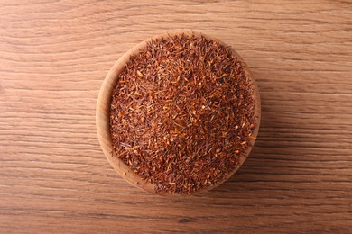 Dry rooibos leaves in bowl on wooden table, top view