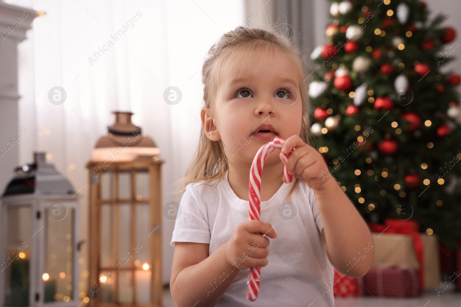 Photo of Cute little girl with candy cane in room decorated for Christmas