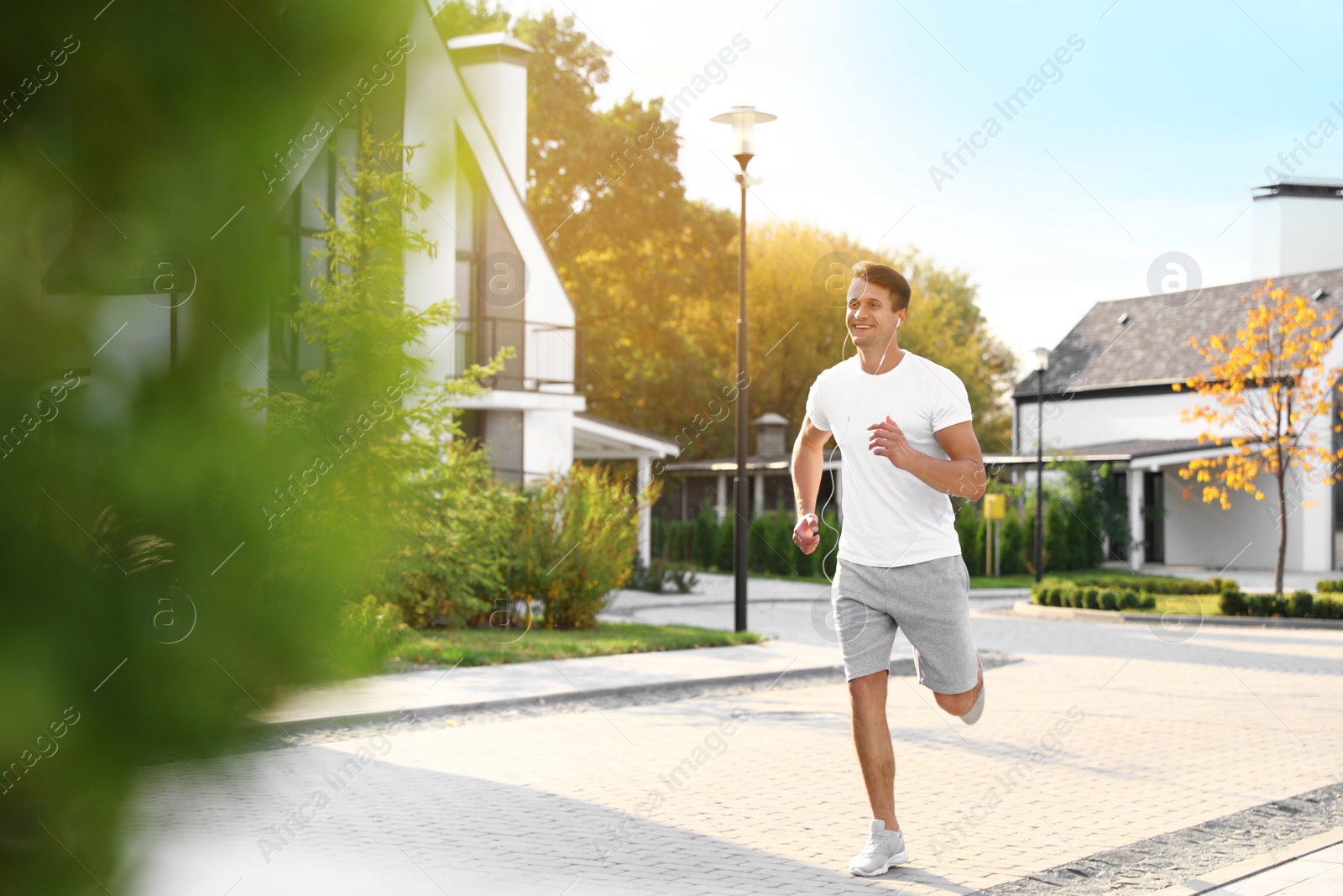 Photo of Young man with earphones running outdoors on sunny morning. Healthy lifestyle