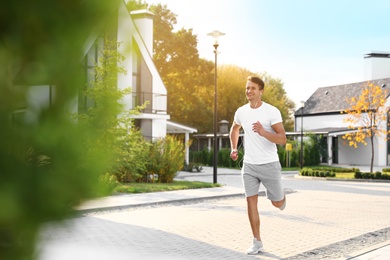 Young man with earphones running outdoors on sunny morning. Healthy lifestyle