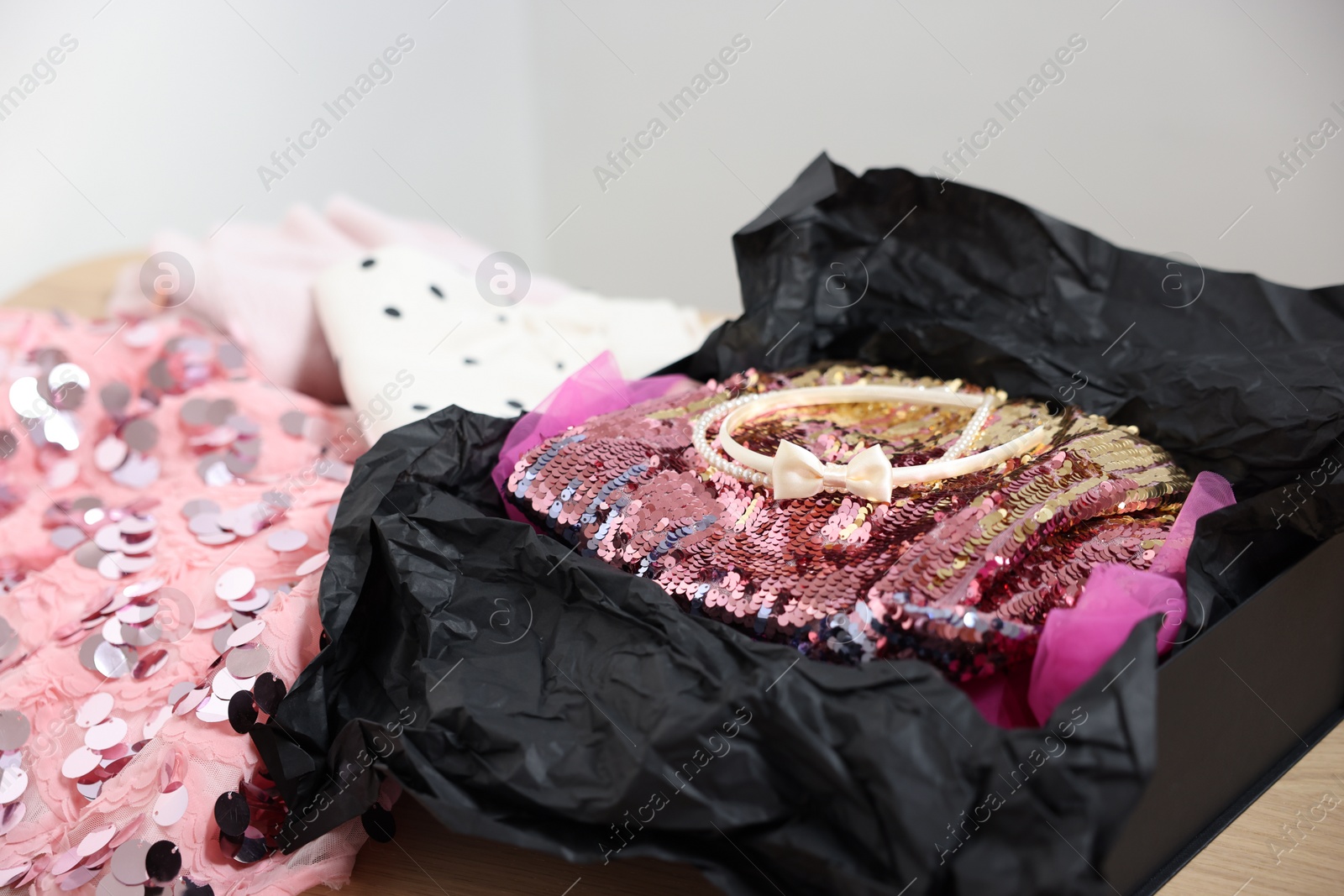 Photo of Headbands and stylish pink carnival costume with sequins in black box on table, closeup