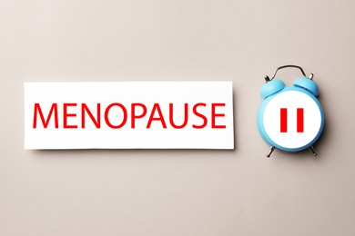Menopause word and alarm clock with pause symbol on beige background, top view