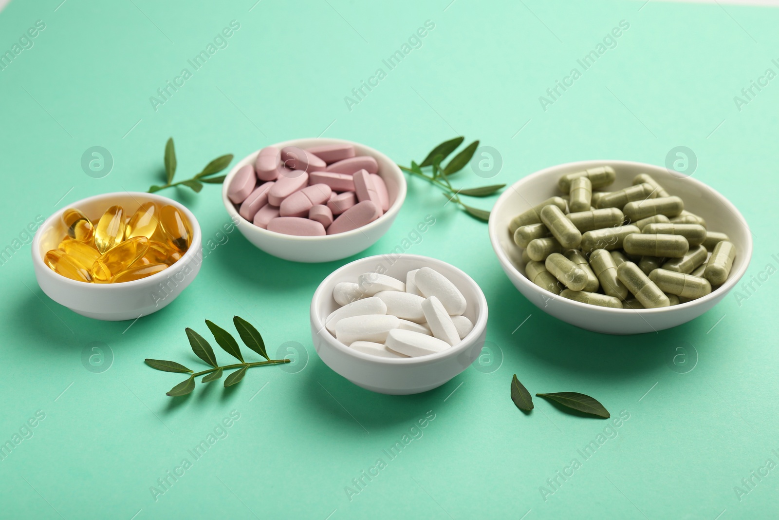 Photo of Different vitamin capsules in bowls and leaves on turquoise background