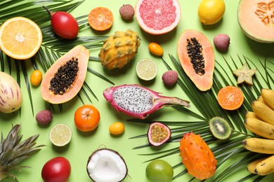Photo of Different exotic fruits and palm leaves on green background, flat lay