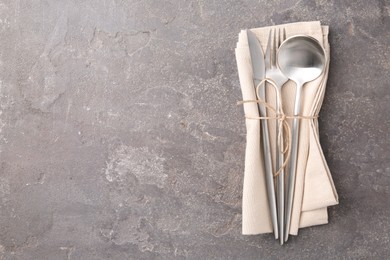 Set of stylish cutlery and napkin on grey textured table, top view. Space for text
