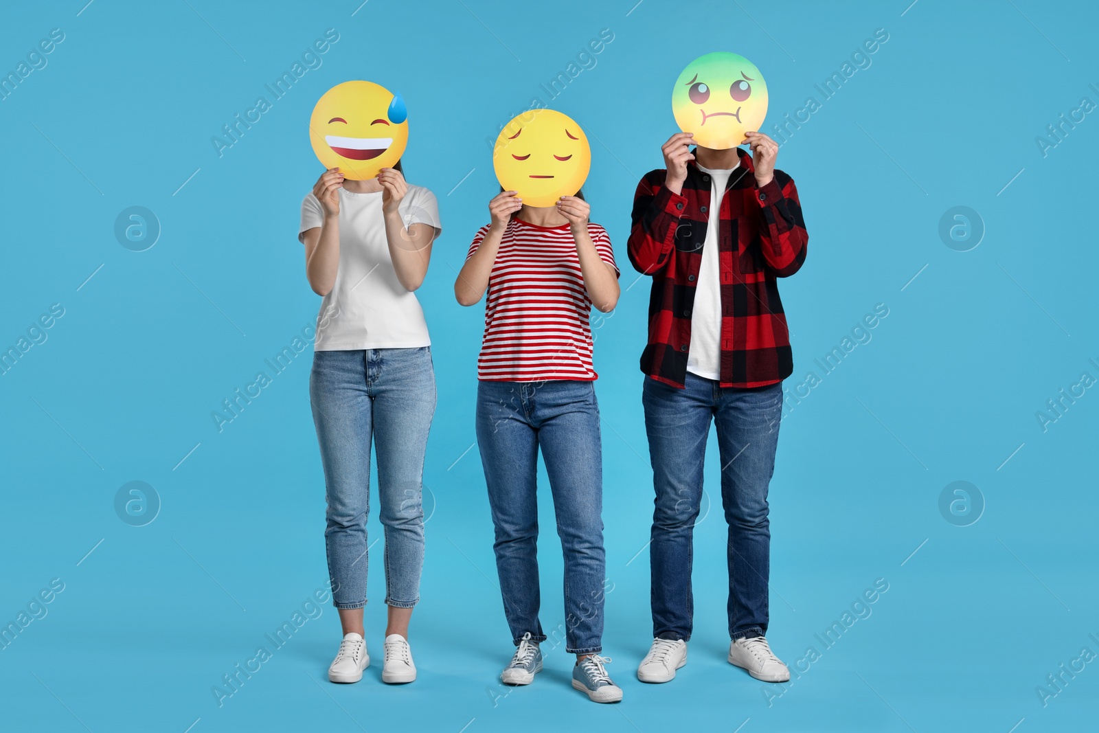 Photo of People covering faces with emoticons on light blue background