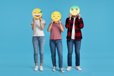 People covering faces with emoticons on light blue background