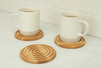 Photo of Hot beverage in mugs and stylish wooden cup coasters on white table