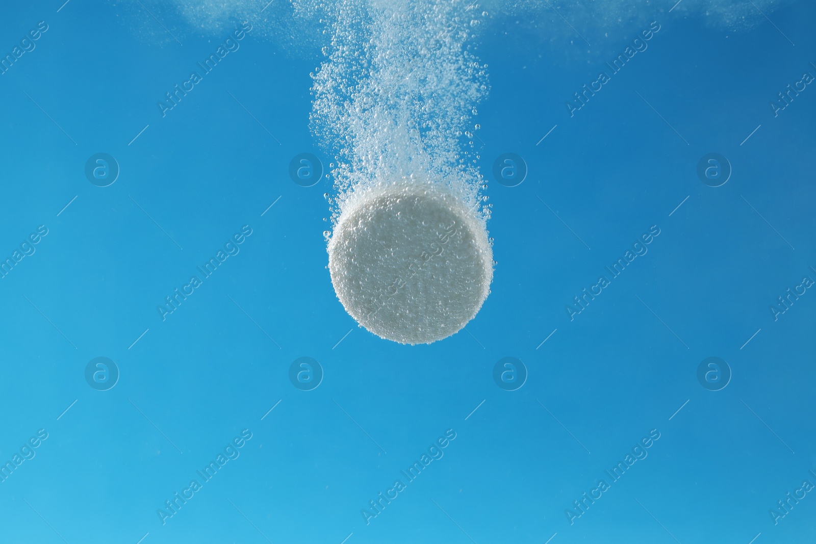 Photo of Effervescent pill dissolving in water on light blue background, closeup