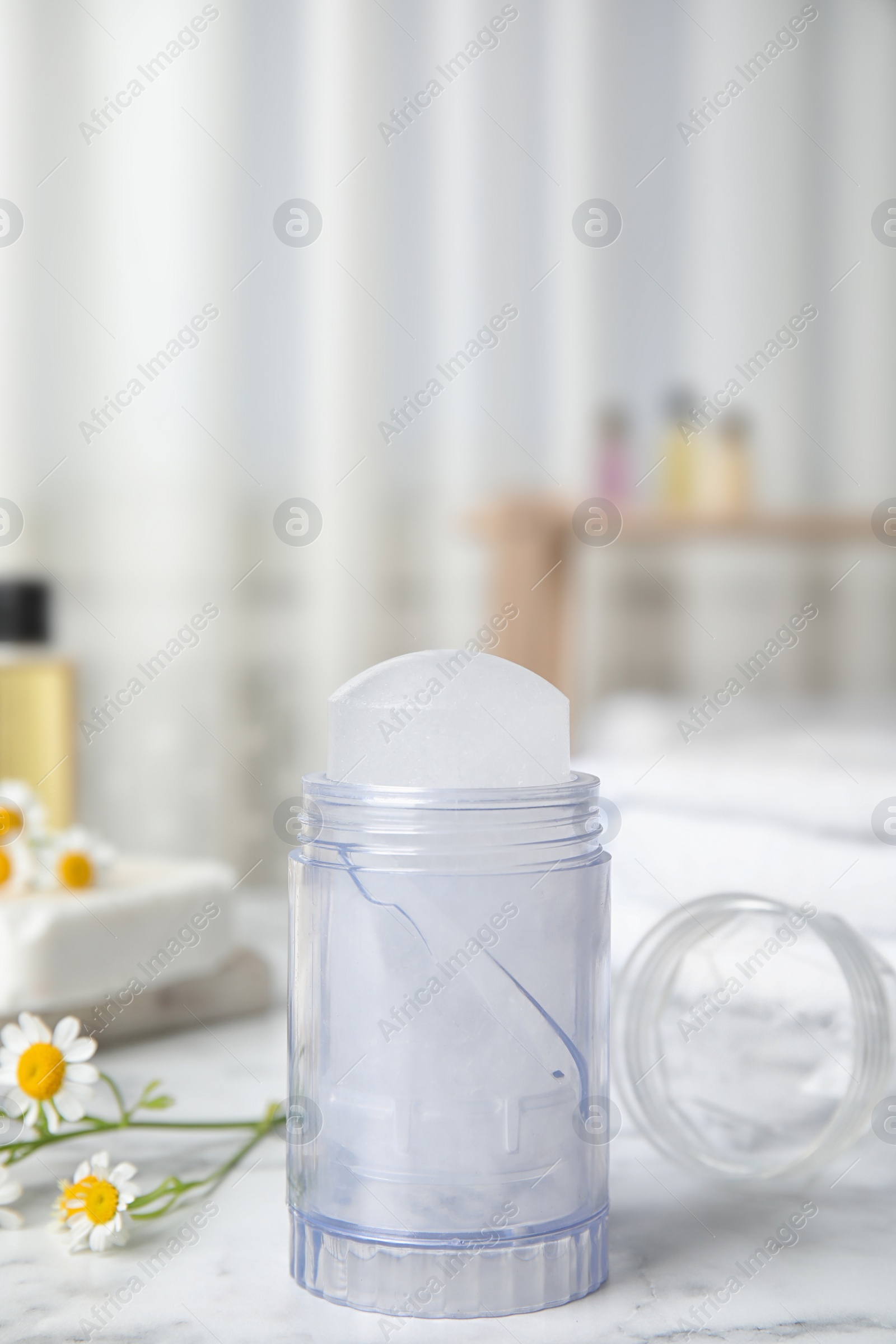 Photo of Natural crystal alum deodorant and chamomile flowers on white marble background