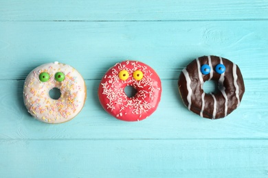 Photo of Delicious donuts decorated as monsters on light blue wooden table, flat lay. Halloween treat