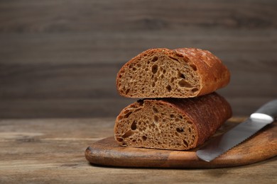 Photo of Cut rye baguette with knife on wooden table. Space for text