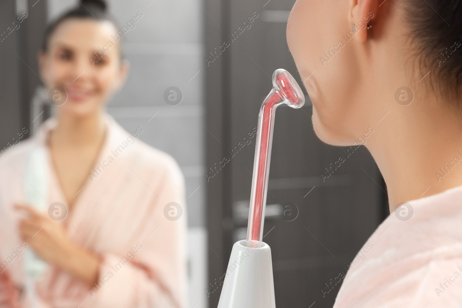 Photo of Woman using high frequency darsonval device near mirror in bathroom, closeup. Space for text