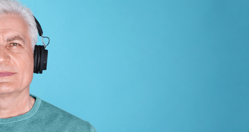 Image of Mature man listening to music with headphones on blue background, space for text. Banner design