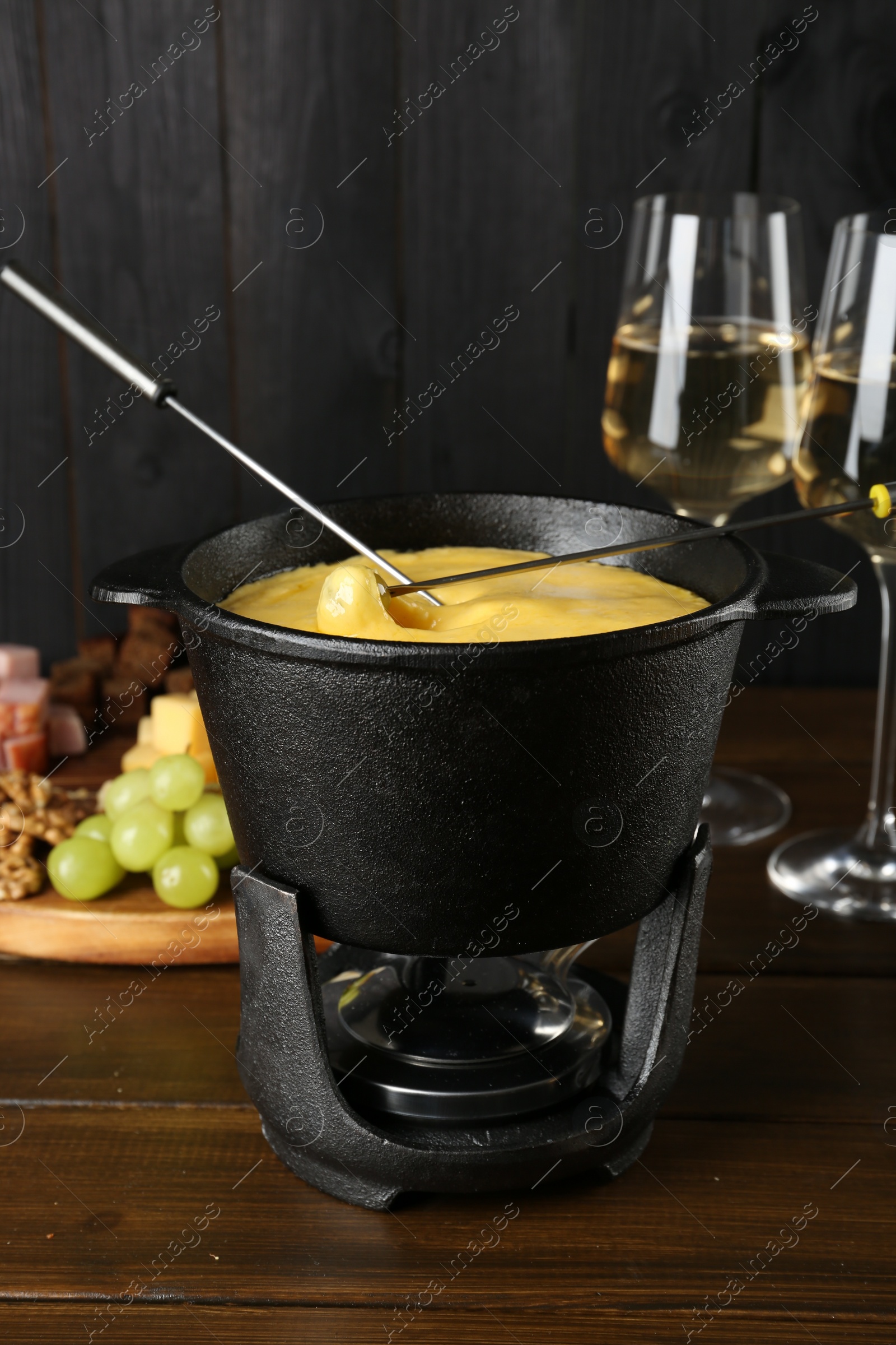 Photo of Dipping different products into fondue pot with melted cheese on wooden table