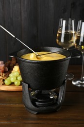 Dipping different products into fondue pot with melted cheese on wooden table