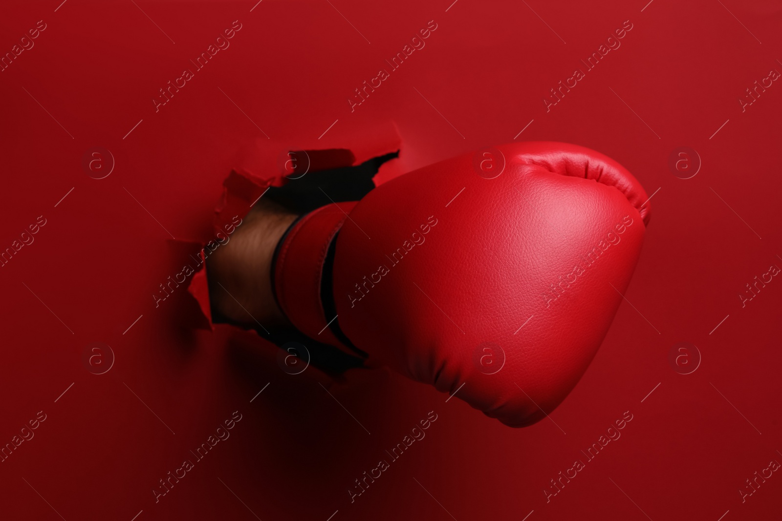 Photo of Man breaking through red paper with boxing glove, closeup