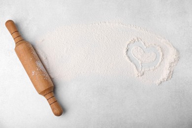 Photo of Heart made of flour and rolling pin on light grey table, top view