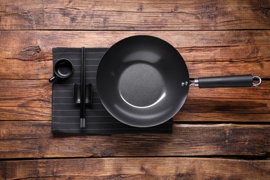 Photo of Empty iron wok, sauce bowl and chopsticks on wooden table, flat lay