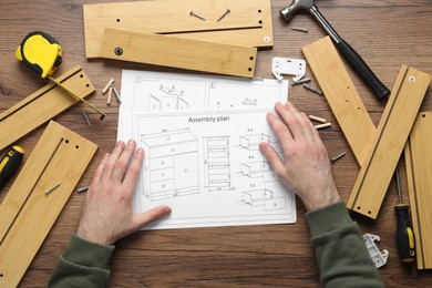 Man with furniture and assembly plan at wooden table, top view