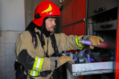 Photo of Firefighter in uniform with fire engine equipment at station