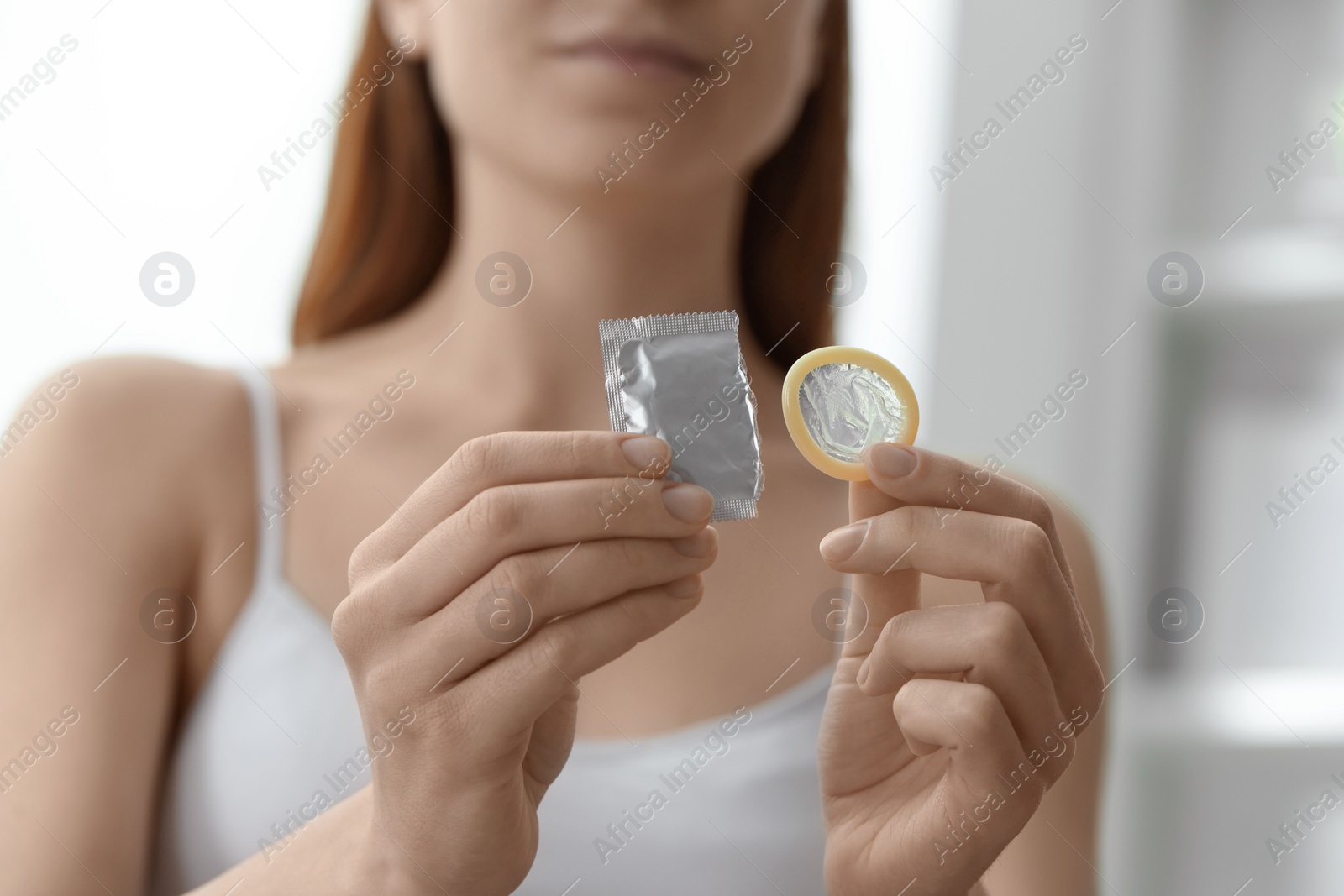 Photo of Woman holding unwrapped condom indoors, closeup. Safe sex